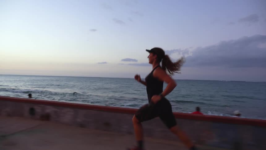 Woman runs along coastal sidewalk passing pedestrians and people standing on the beach