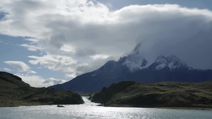 River leads from ocean between vegetation shores to mist covered snow capped mountains