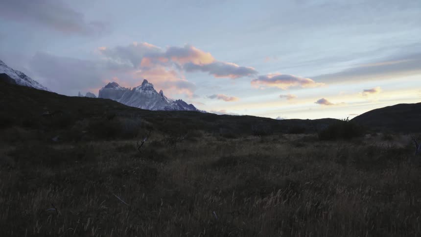 Grass blowing in the wind and mountains in the distance under a cloudy sky