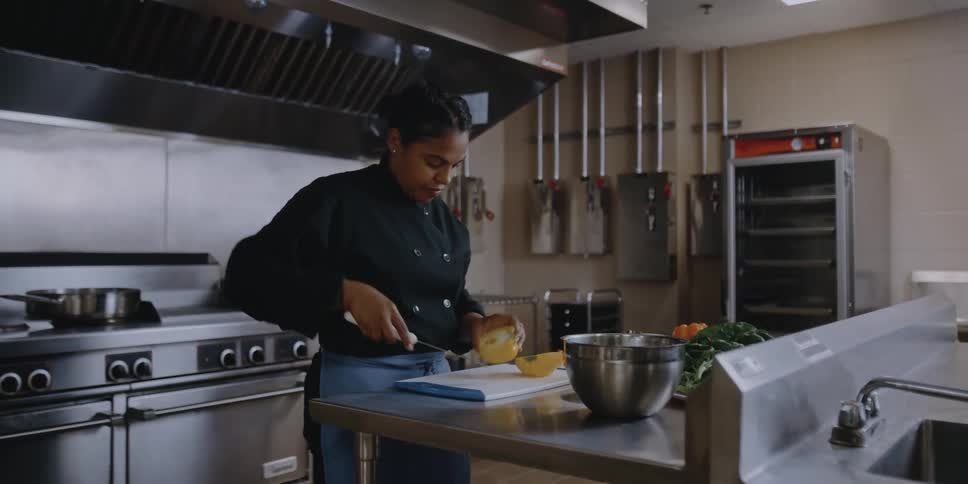 A woman in a kitchen cutting a vegetable with a knife on a cutting board