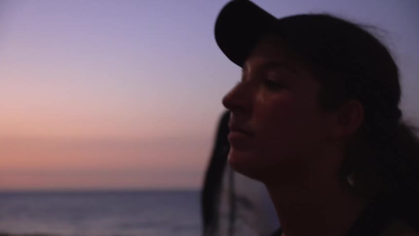 A sweaty woman with curly hair and wearing a visor walks near to a tranquil ocean