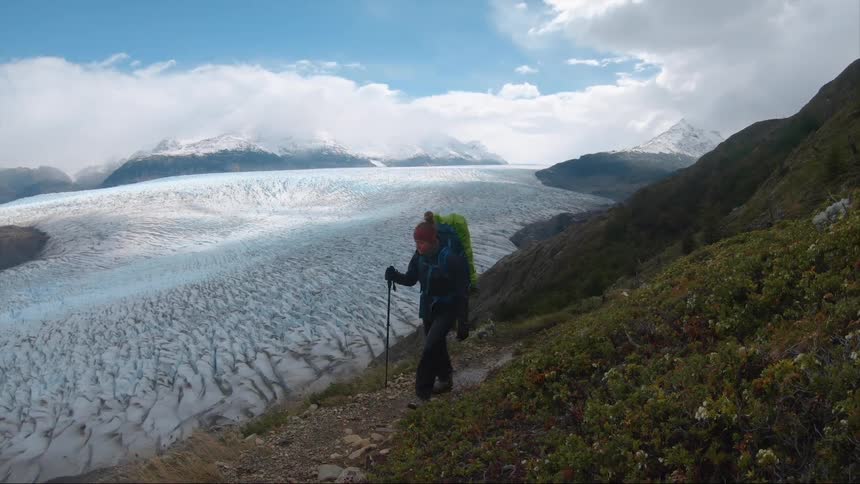 A woman hikes along a narrow path on a mountain slope overlooking a frozen valley