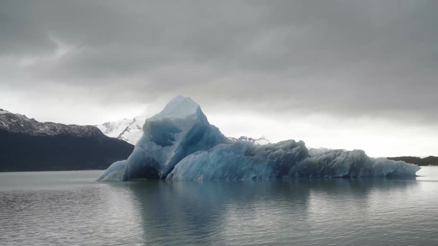 An iceberg in the water and snow covered mountains in the distance