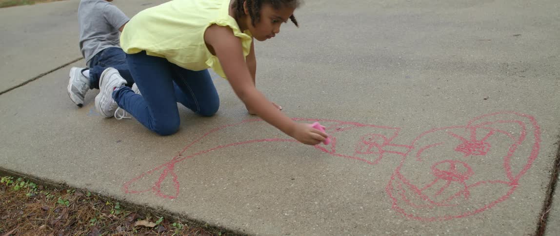 Girl drawing with pink chalk on the sidewalk on a park