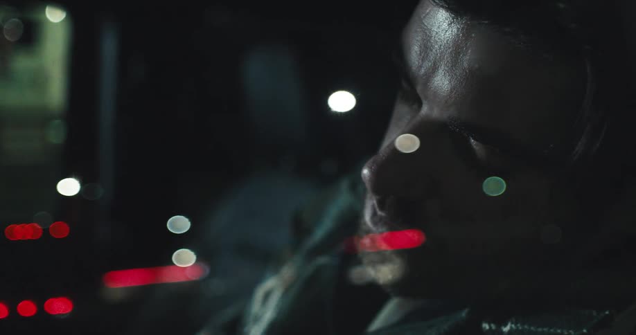 A man rests with his head near a glass window upon which red lights are reflecting