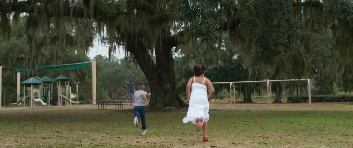 A brother and sister hold hands and then race each other across a playground