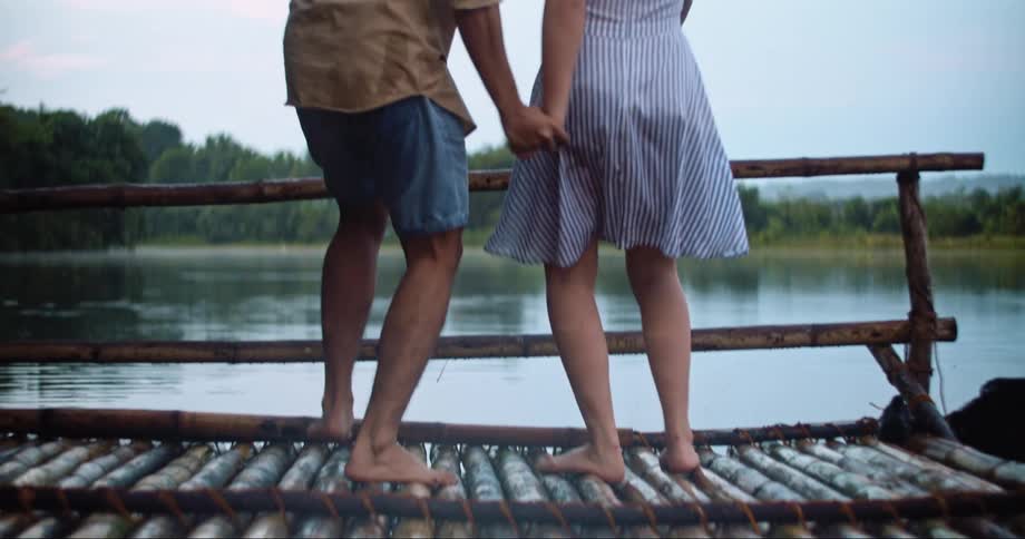 A young man and woman playfully run to the edge of a dock at overlooks a large river
