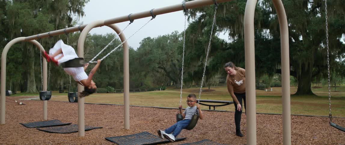 A couple of children smile as they swing high on a swing set with help from an adult