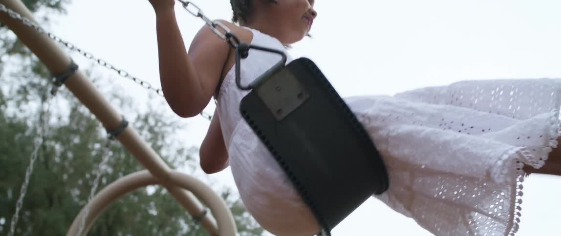 Mother pushing daughter and son on swings in the playground