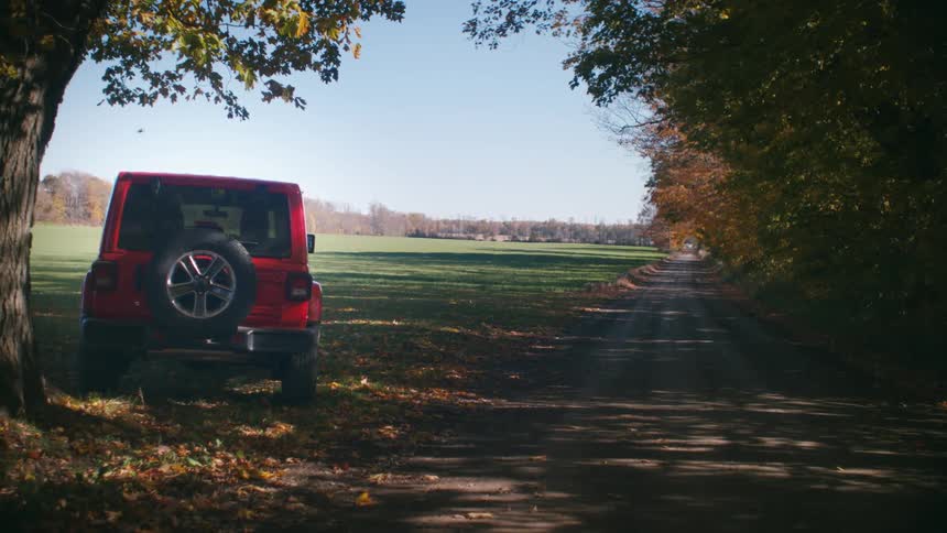 Red car under the autumn tree next to the dirt road