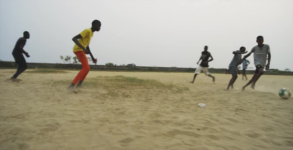 A group of boys running and playing soccer in a dirt field outside