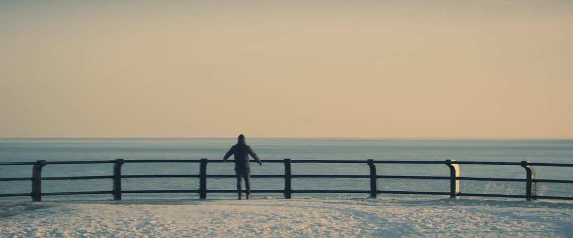 A man standing near the water on a winter day