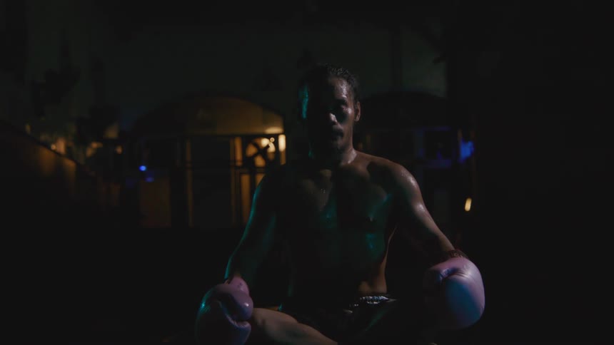 Male muscular fighter with gloves sits cross legged on the ground