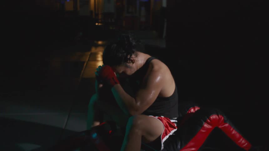 Man wearing sports clothes sits tiredly on the floor of a gym