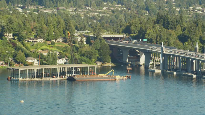 Cars travel in both direction on a bridge over water with a shipping crane on a platform nearby
