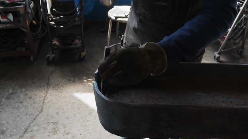 A person with gloves a hammer and chisel shaping a piece of metal in a workshop
