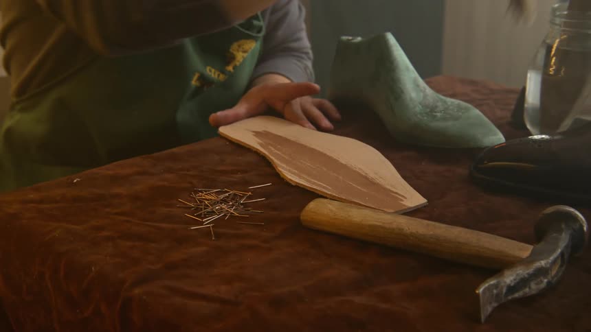 A shoemaker brushes a stain onto the bottom of a sole