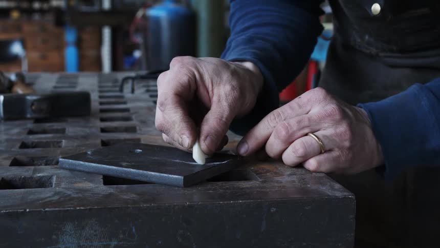 A man traces an outline with chalk on a cement block in his workshop