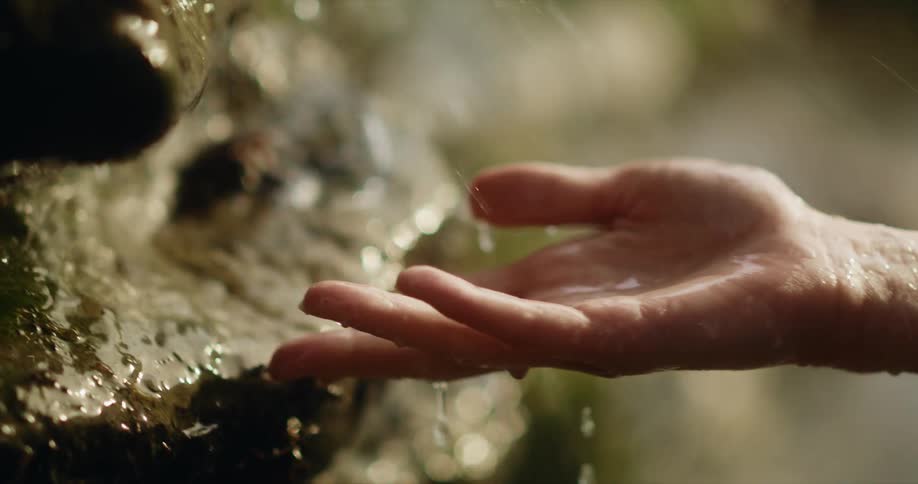 A woman holds her hand next to rocks as rain falls down