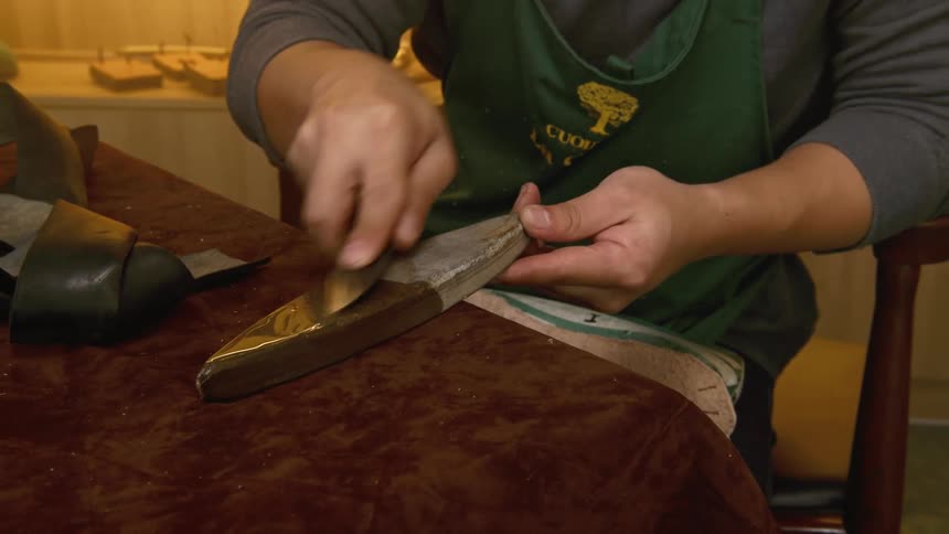 A leather shoemaker uses a blade to scrape a metal object
