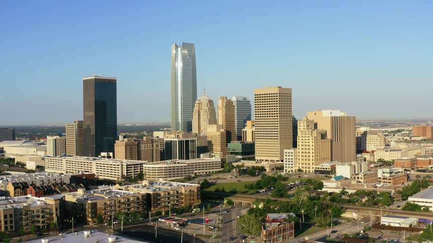 Cars travel on city streets with a city skyline behind on a blue sky day