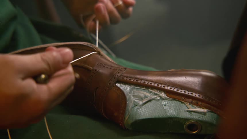 Cordwainer threading the sole of a leather shoe