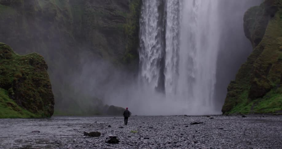 Man walking away from a large waterfall