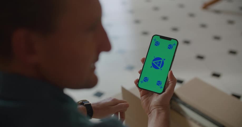 Man with a blue shirt and a wristwatch holds iphone smartphone with green screen