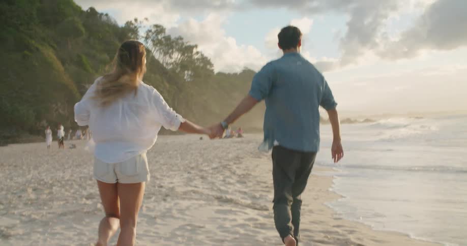 A couple happily hold hands as they run along a sandy beach on a sunny day