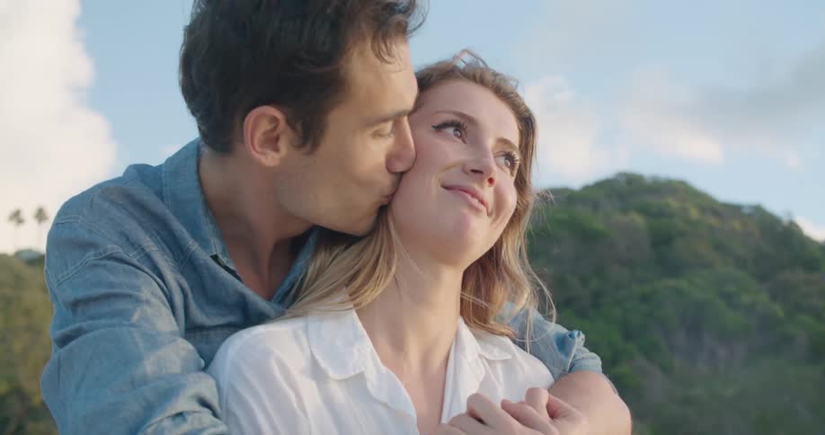 A man hugging a smiling woman and kissing her cheek outside