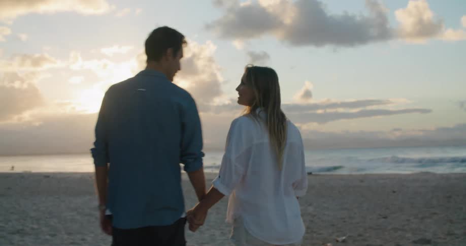 Couple walk along beach hand in hand pausing to share a kiss