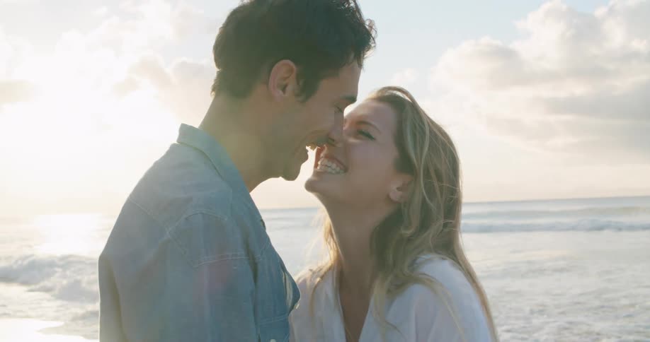 A couple is kissing on a beach with sea behind them