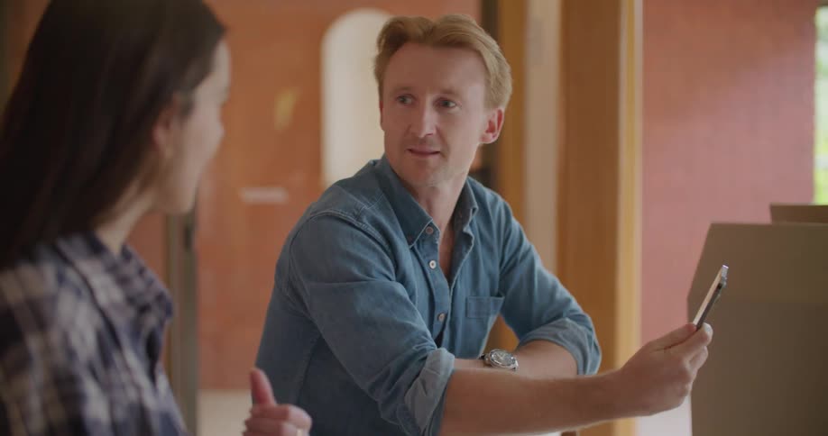 A man holds a cell phon while talking with a woman