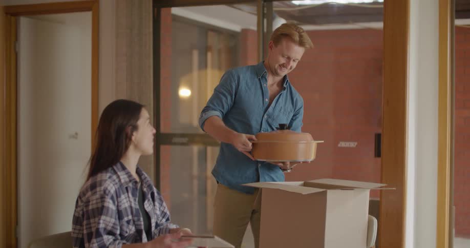 A woman reads a brochure while a man unpacks a covered pot from a cardboard box