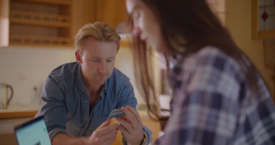 Couple shopping online on a laptop over the kitchen table at home