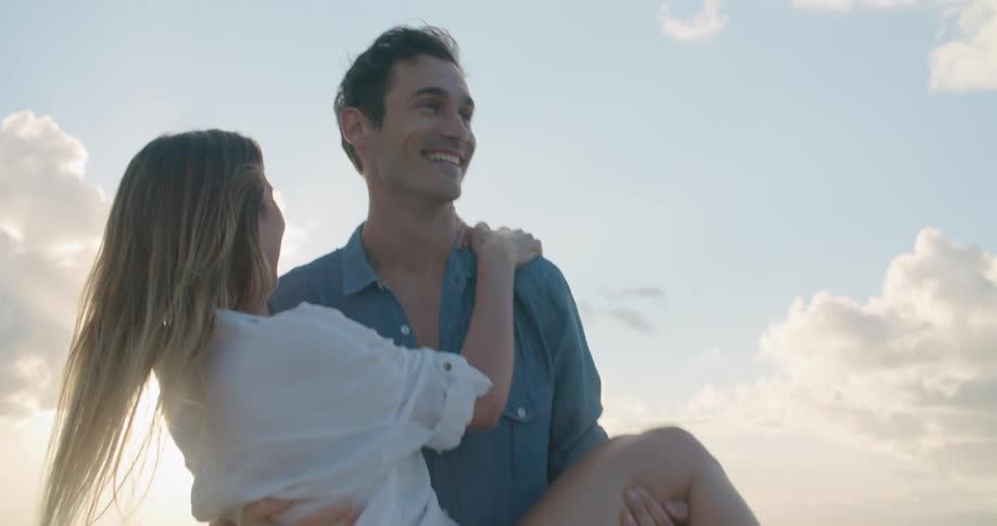 A man carries his wife on the beach as they laugh and smile