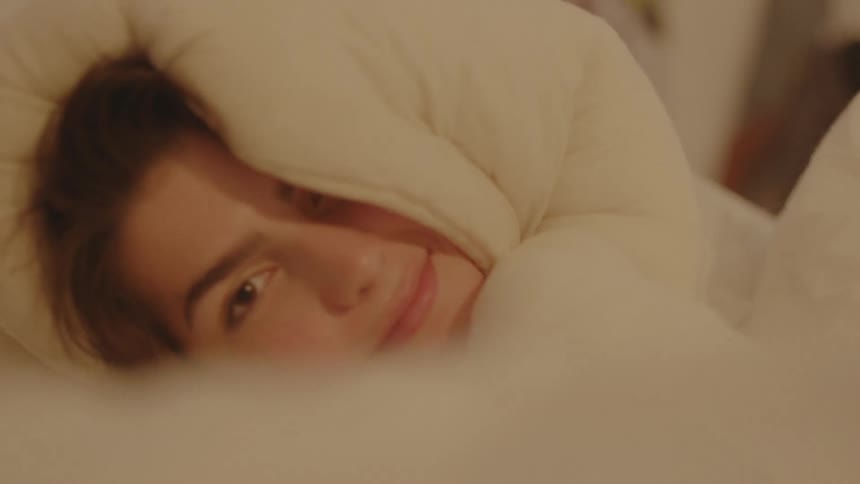 A woman lying down with a blanket wrapped around her body and head with face showing
