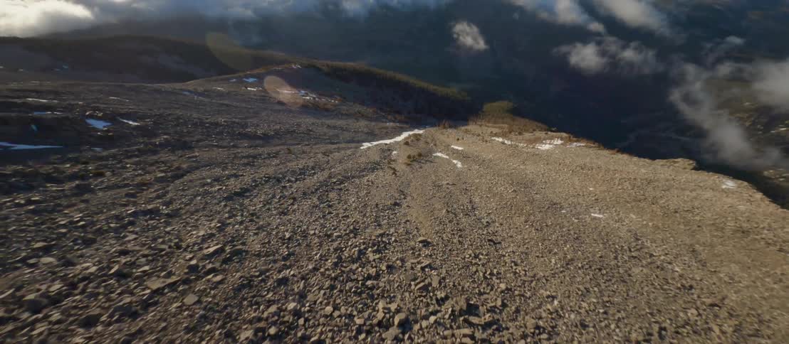 Moving rapidly down a mountain slope dotted with snow rock and brush