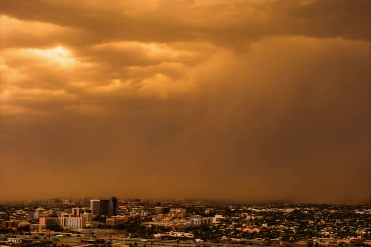 Lightning strikes from storm front moving over city as traffic passes along highway near downtown