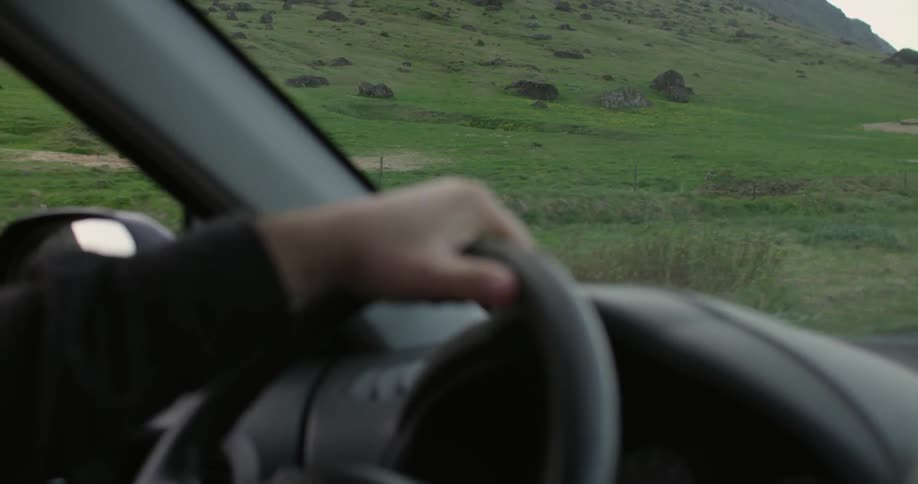 A person with their hand on the steering wheel as they drive during the day