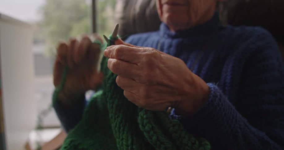 An elderly woman is sewing a blanket indoors