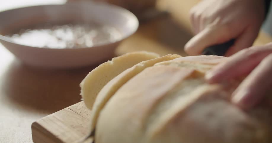 A person with a knife cutting bread on a cutting board on a table