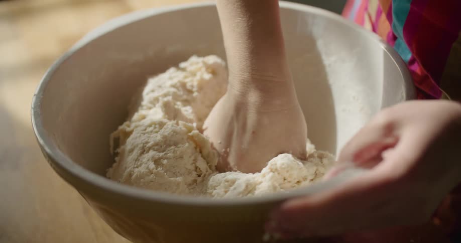 A person kneading dough in a ceramic bowl
