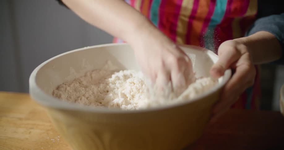 Hands mix and blend flour in a bowl making dough