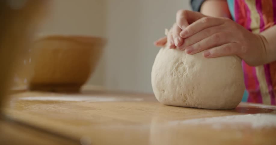 A person in a room kneading dough on a table with flour