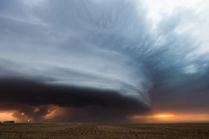 Lightning strikes through dense clouds as a storm moves over a field