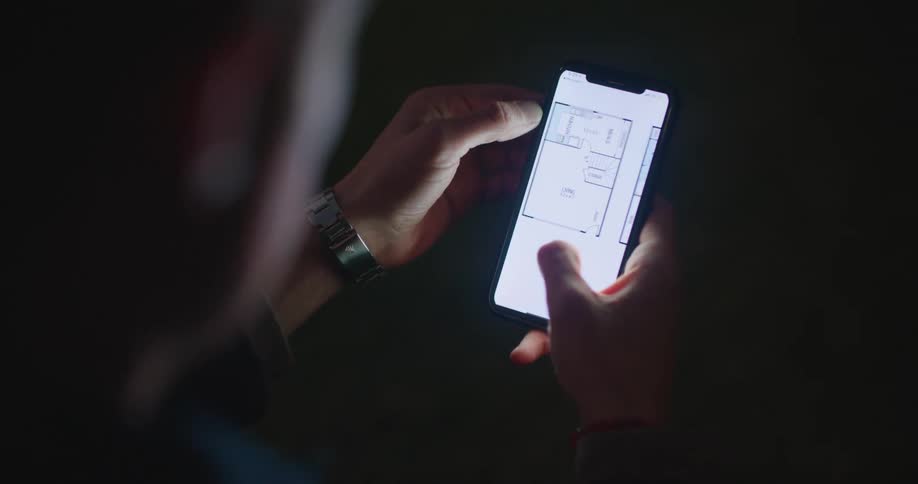 A person scrolls a floor plan on a smartphone in a dimly lit area