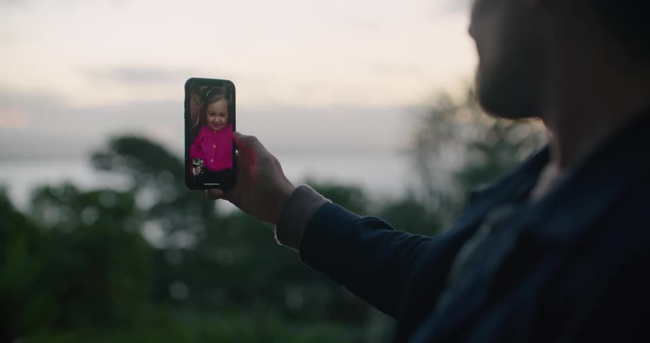 Man talking to a baby girl on a video call on his smartphone at sunset