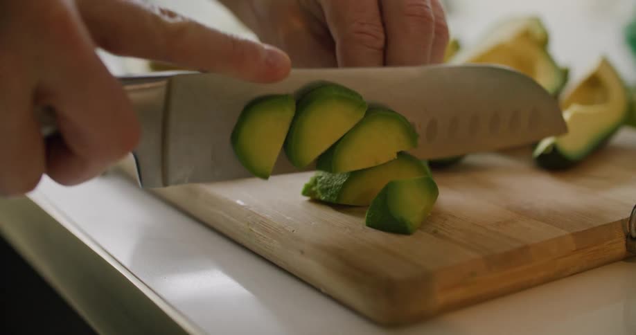 Mans hands cut avocado on the cutting board in the kithchen