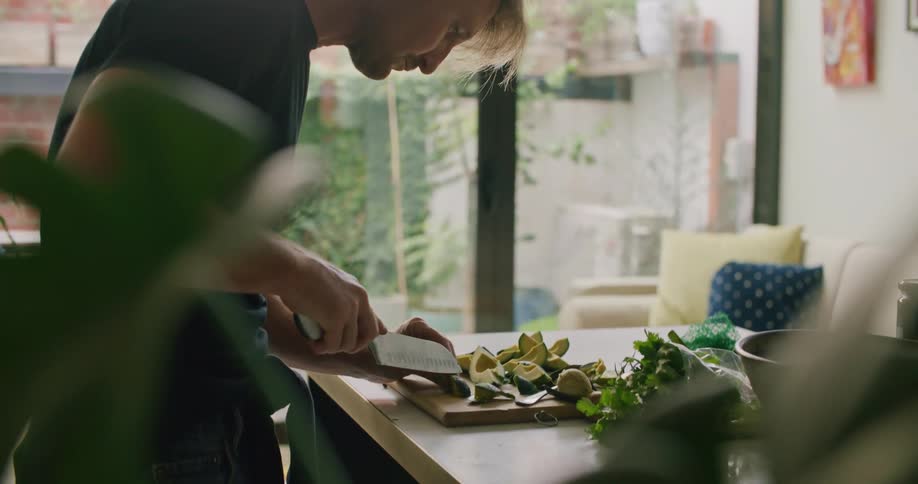 Blonde man with a black t shirt cuts avocado on the cutting board in the kitchen